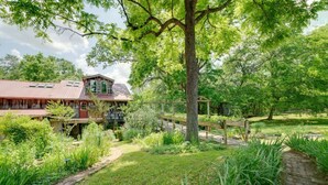 A rustic cabin with a red roof, surrounded by lush greenery and a wooden deck.
