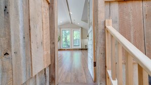 A wooden interior hallway with a staircase leading to a room with large windows and a view of greenery outside.