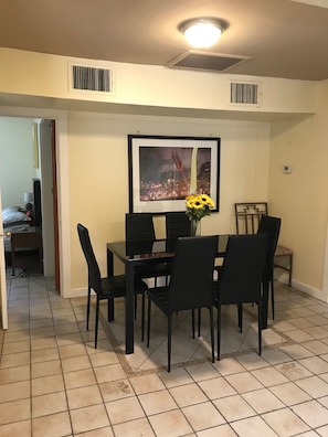 Enjoy meals in this dining area with a table and six chairs, a framed cityscape above, and a door leading to another room.