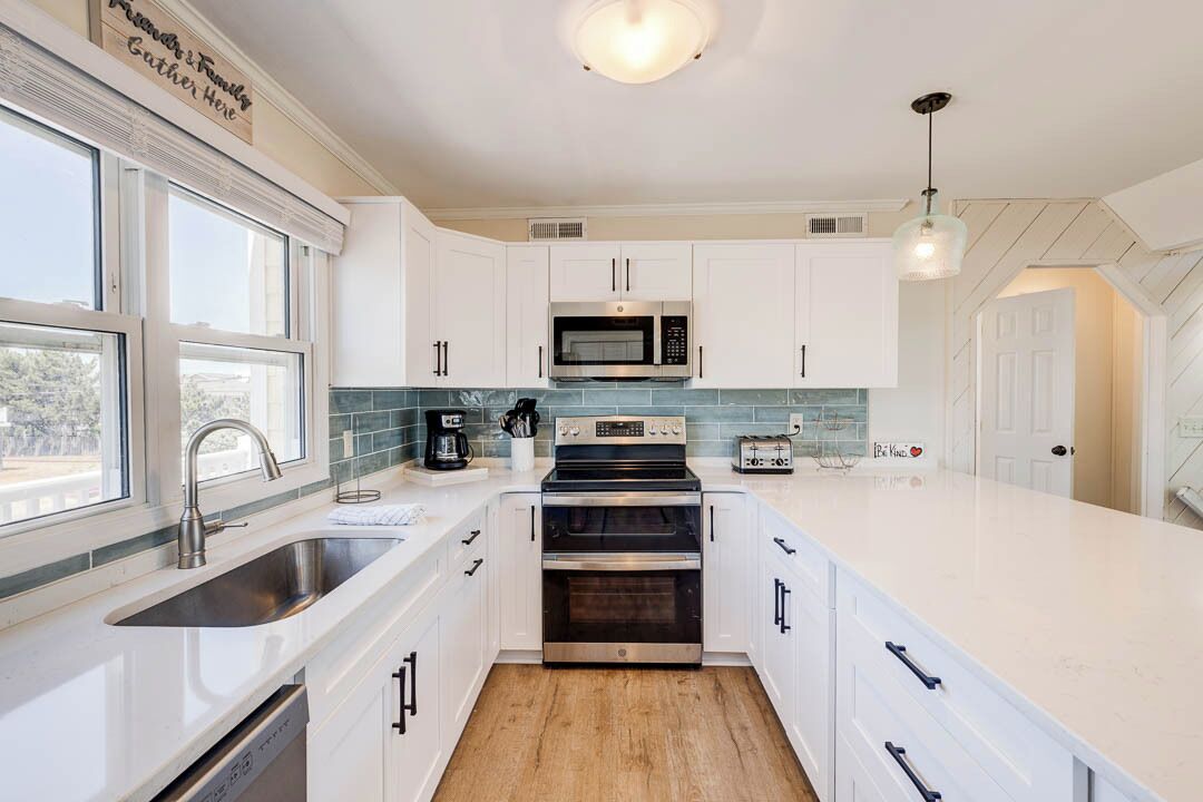 A modern kitchen with white cabinetry, a stainless steel sink, a microwave, a stove, and a toaster.