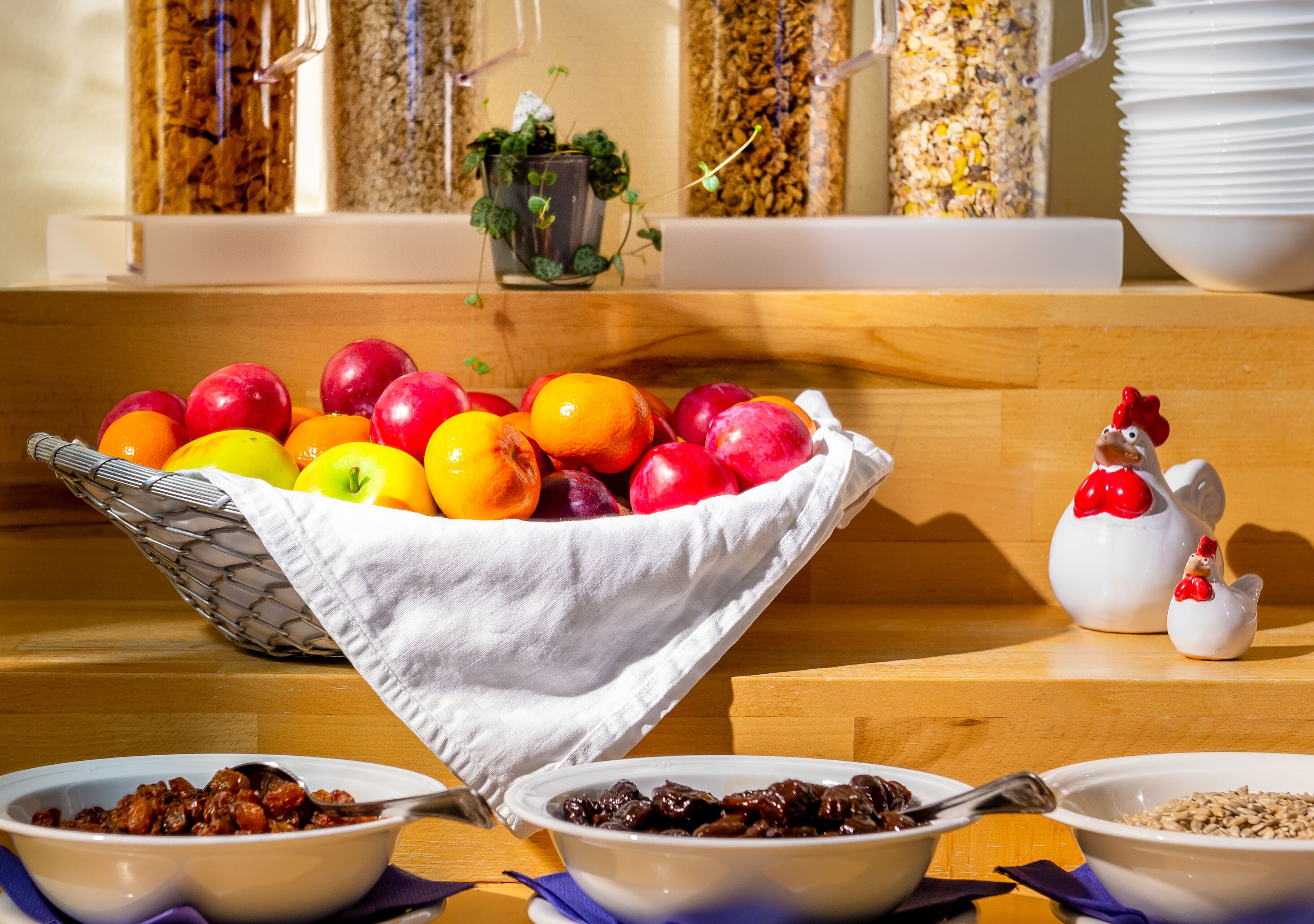 A breakfast buffet with a fruit bowl, cereal, and a decorative chicken figurine.