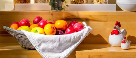 Un bufé de desayuno con un tazón de fruta, cereales y una figurita decorativa de gallina.