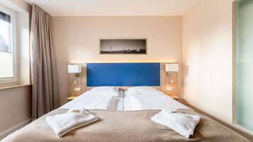 Ein Hotelzimmer mit einem großen Bett, zwei Nachttischen, einem blauen Kopfteil und einem gerahmten Bild an der Wand.