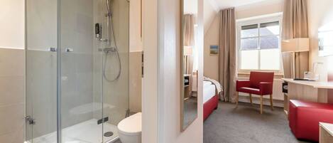 A modern bathroom with a glass-enclosed shower, a toilet, and a bed with a red chair.