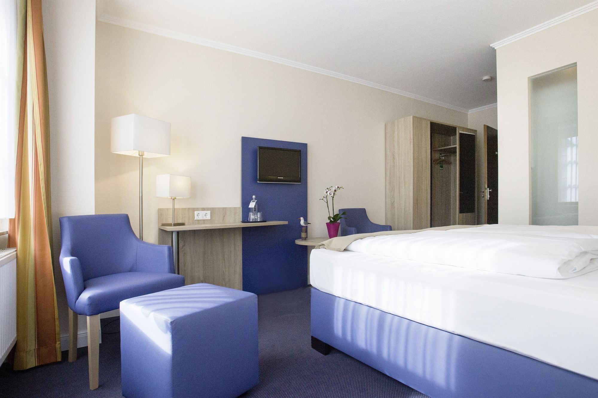 Hotelkamer met een bed, een bureau, een stoel, een bijzettafeltje, een lamp en een potplant.