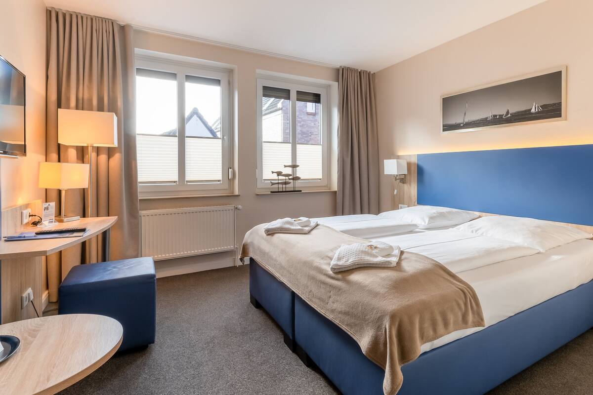 A hotel room with a bed, a desk, a chair, and a window with curtains.