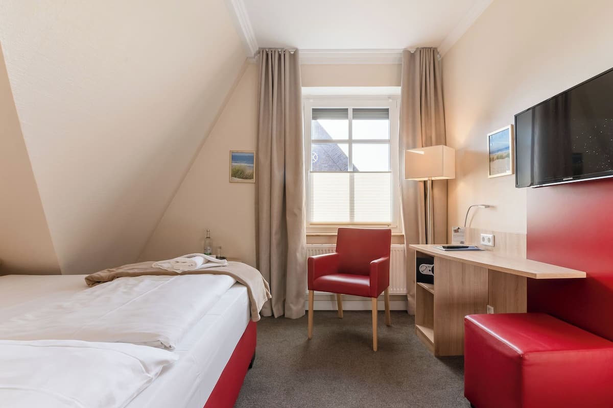 A hotel room with a bed, a desk, a chair, a TV, and a window with curtains.