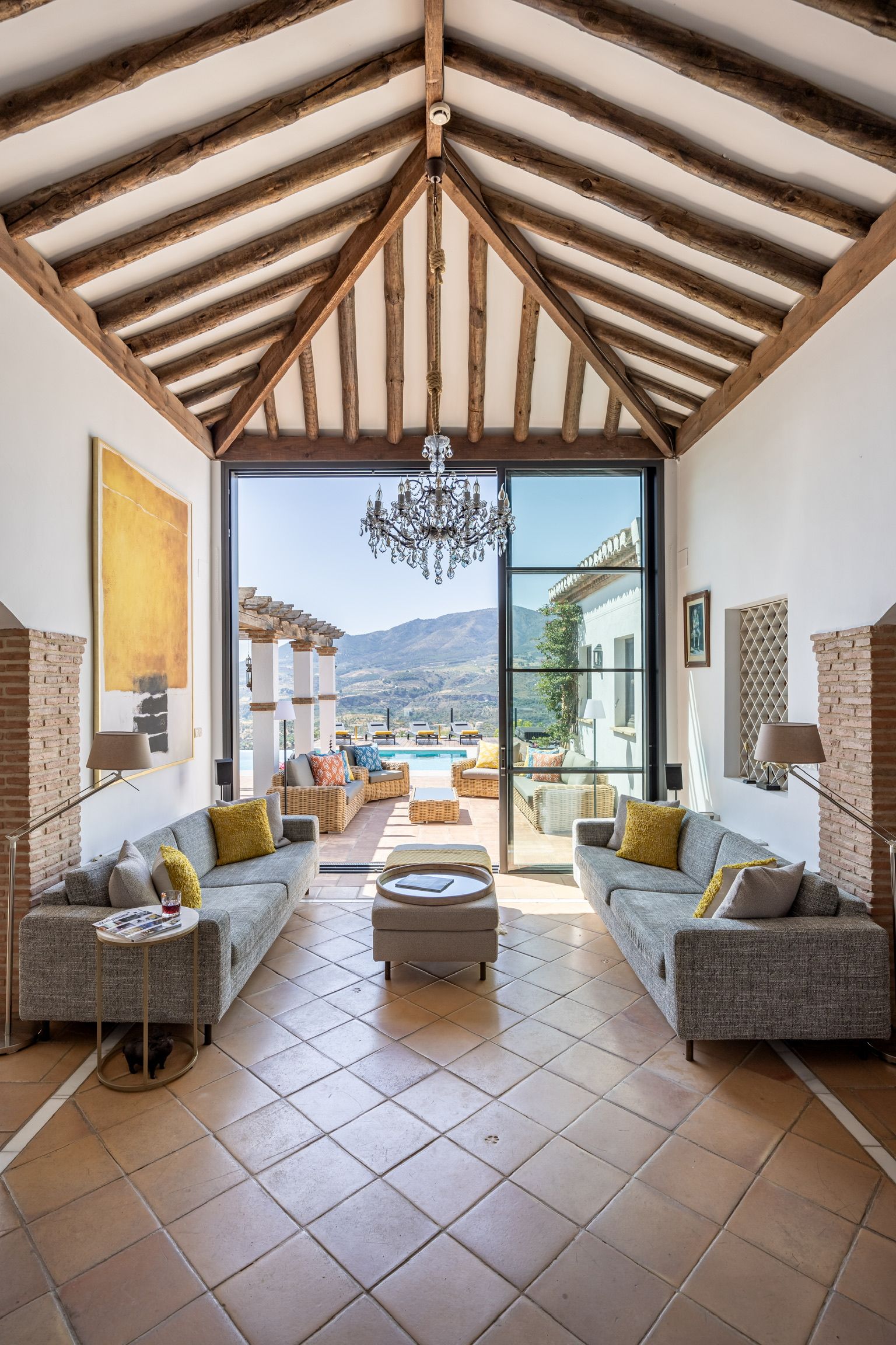 Un salon spacieux avec un plafond haut, de grandes fenêtres et une vue sur une piscine et des montagnes.