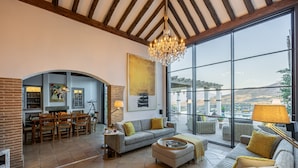 A spacious living area with a large window, a chandelier, and a fireplace. - Exclusive Country Villa with Stunning Views & Infinity Pool (Restabal)