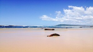 Uma praia com céu claro, águas calmas e uma montanha ao longe.