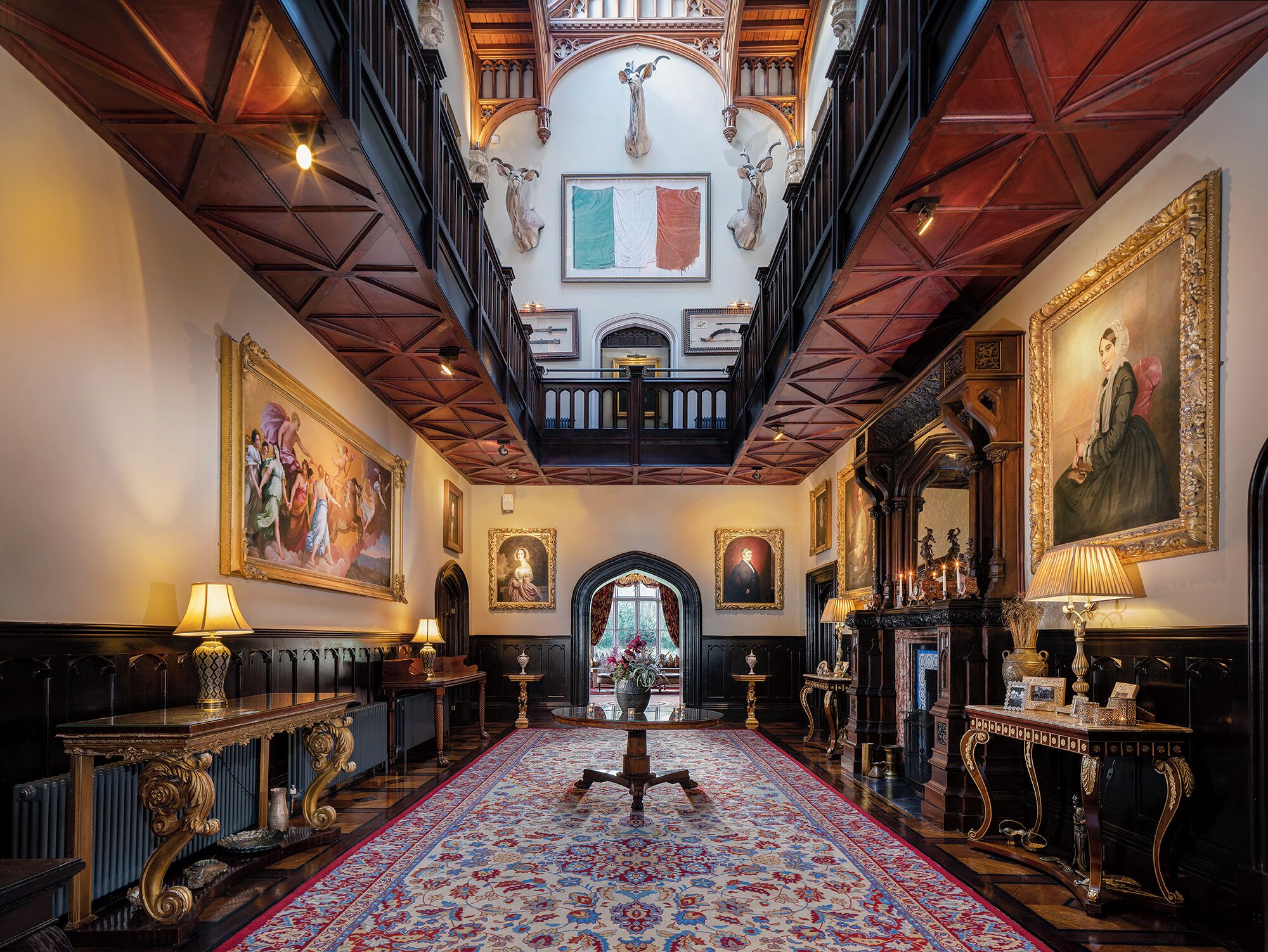 A grand hallway with ornate woodwork, a large chandelier, and a red carpet leading to a grand staircase.