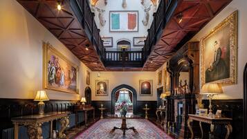 A grand hallway with ornate woodwork, a large chandelier, and a red carpet leading to a grand staircase.