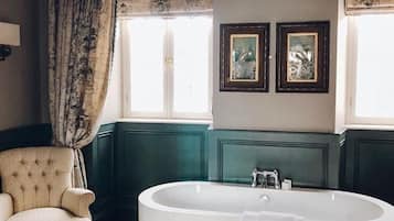 A bathroom with a freestanding bathtub, a chair, and two framed pictures on the wall.