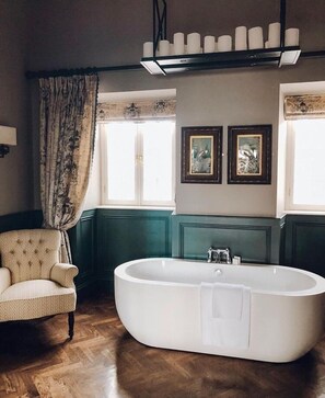 A bathroom with a freestanding bathtub, a chair, and two framed pictures on the wall.