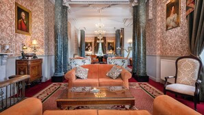 A grand room with a chandelier, ornate columns, a sofa, and a chair.