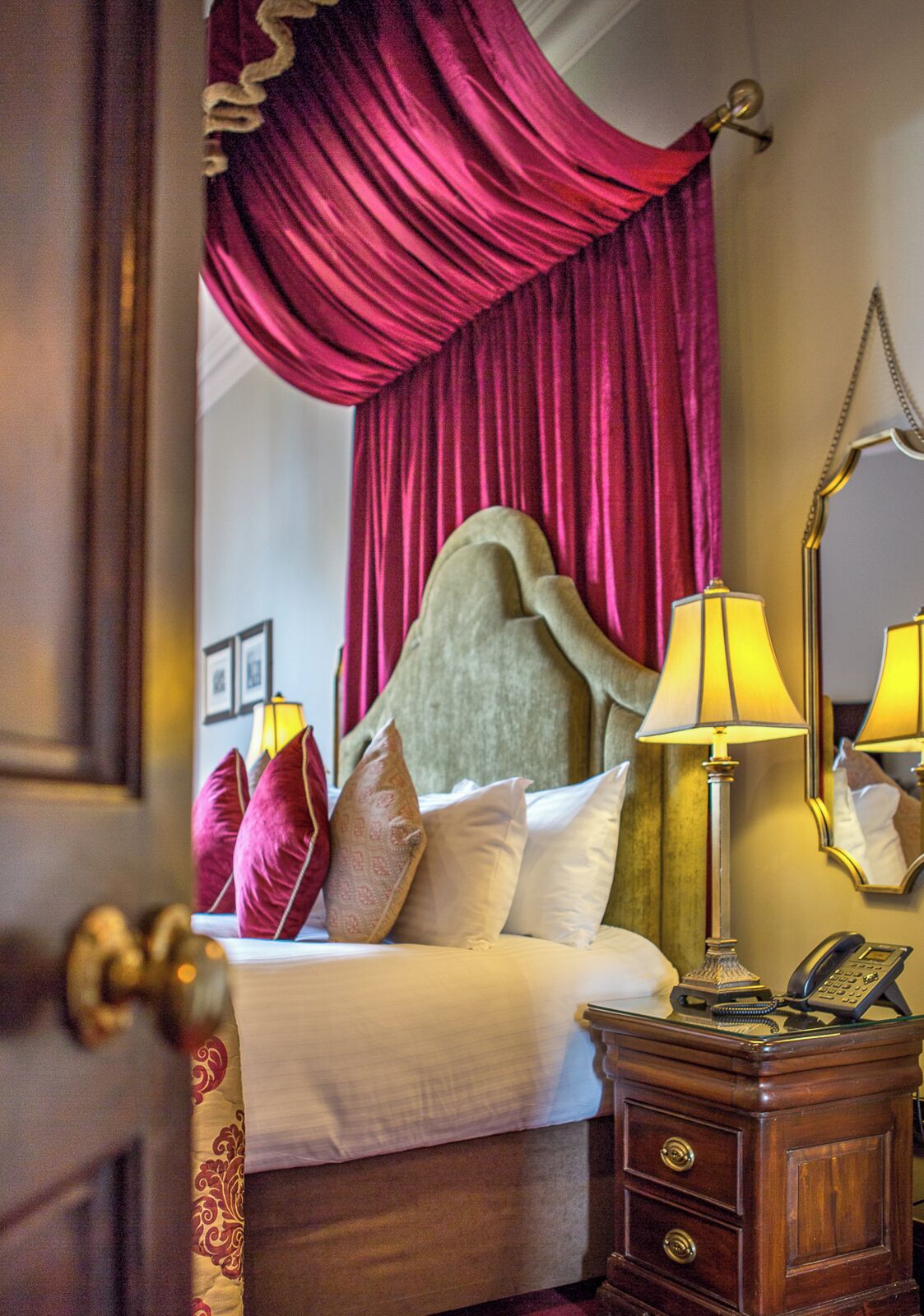 Une chambre d’hôtel avec un lit, une table de chevet avec une lampe, un téléphone et un miroir.