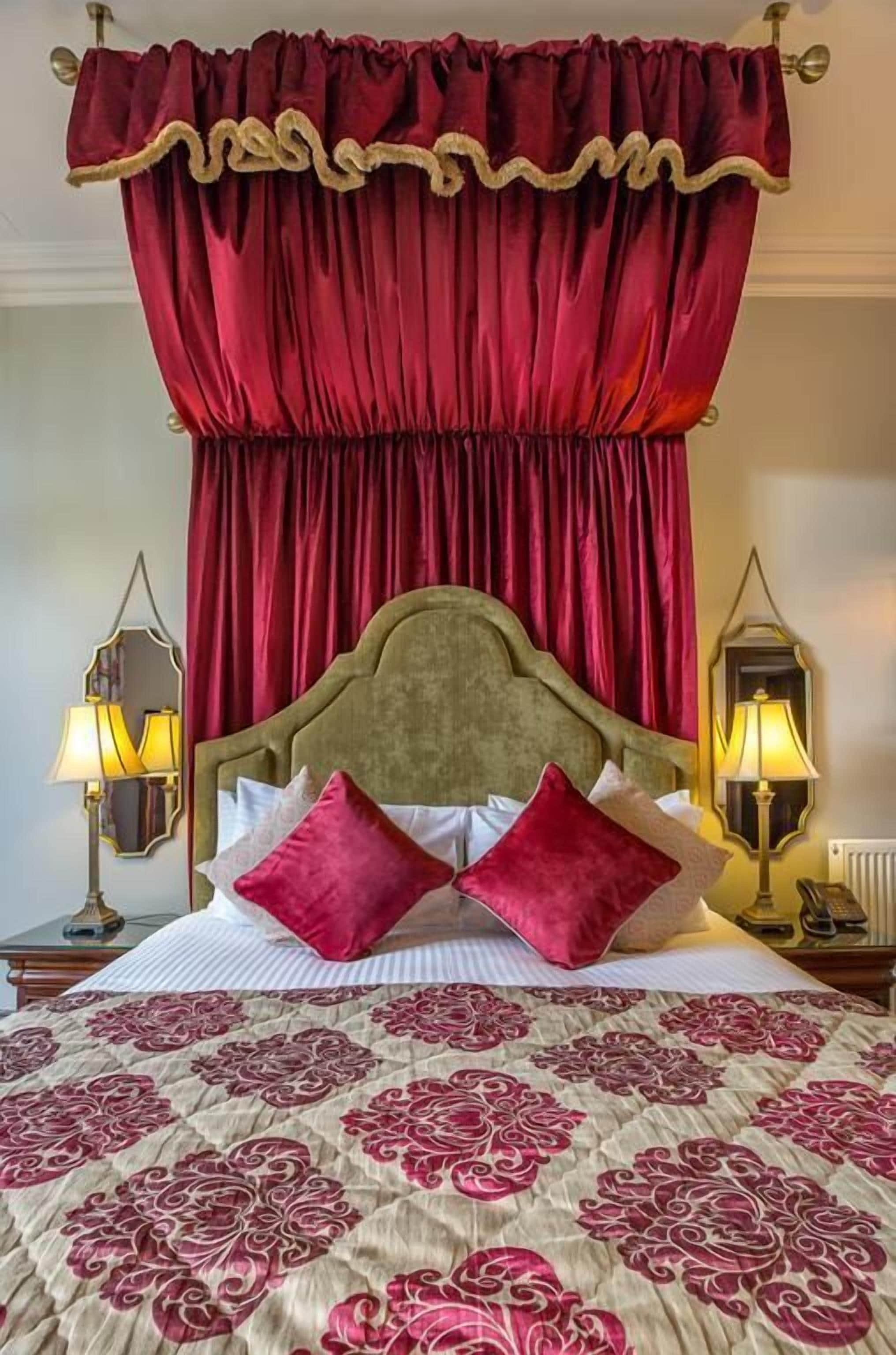 Quarto com cama grande, cortinas vermelhas e duas luminárias fixadas na parede.