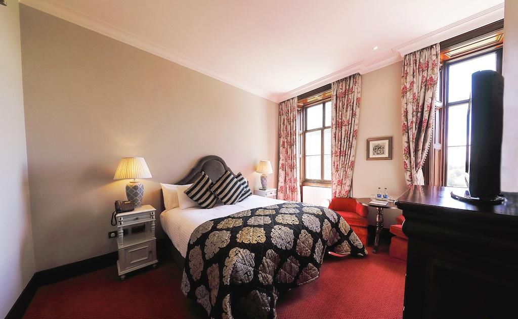 A hotel room with a bed, bedside tables, a desk, a chair, and a TV.