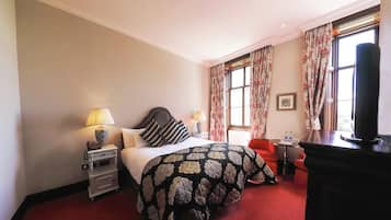 A hotel room with a bed, bedside tables, a desk, a chair, and a TV.