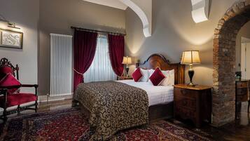 A hotel room with a large bed, a red and gold patterned carpet, a wooden chair, and a brick wall.