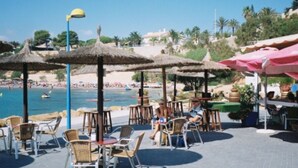 Un café situé en bord de mer, avec une terrasse, des parasols et une vue sur la plage et l’océan.