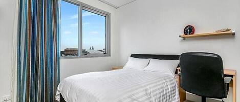 Habitación de hotel con cama, escritorio, silla, ventana con cortinas y un reloj en la pared.