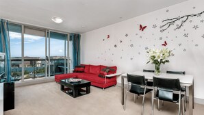 Ein modernes Wohnzimmer mit einem roten Sofa, einem Esstisch mit Stühlen und einem großen Fenster mit Blick auf die Stadt.
