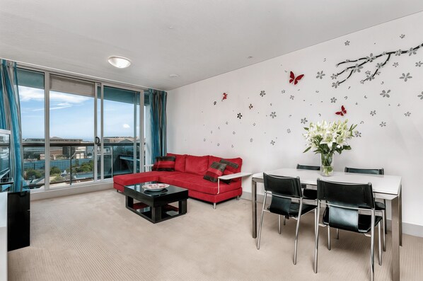 Una sala de estar moderna con un sofá rojo, una mesa de comedor con sillas y un ventanal con vistas a la ciudad.