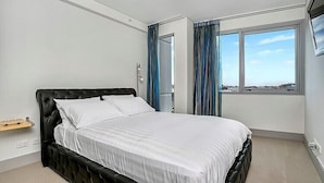 Ein modernes Hotelzimmer mit einem großen Bett, einem kleinen Nachttisch, einem Fenster mit Vorhängen und Blick auf die Stadt.