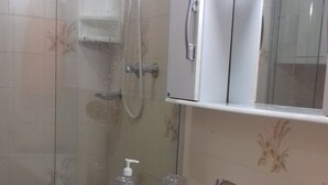 Um banheiro com chuveiro, pia e espelho.