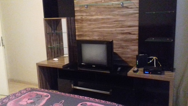 Quarto de hotel com uma unidade de entretenimento em madeira, uma televisão de tela plana, um controle remoto e um pequeno relógio digital.