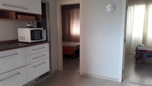Quarto compacto com cozinha compacta, uma cama e uma pequena mesa com toalha colorida.