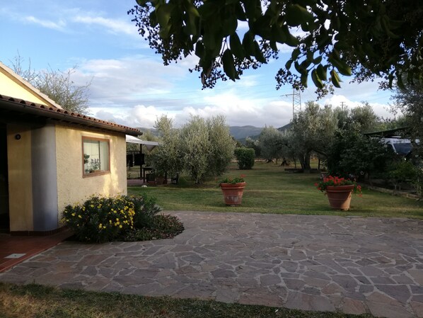 A house with a stone patio, a garden with potted plants, and a view of the countryside.