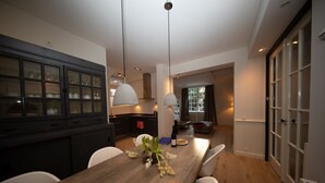 Une cuisine moderne avec une table à manger en bois, des chaises blanches et des luminaires suspendus.