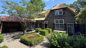 Une maison en briques avec un toit de chaume, un jardin circulaire avec un bassin, et une haie bien entretenue.