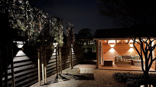Un espace extérieur accueillant, aménagé avec un banc en bois et une table, entouré d’une clôture en bois et de plantes.