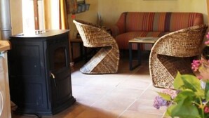 A cozy living room with a fireplace, wicker furniture, and a sofa. - Une Sorcière sur le toit - Gîte** en Aveyron: Countryside and absolute tranquillity! (Firmi)