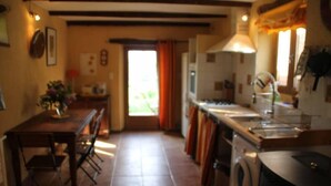 A kitchen with a washing machine, a dining table with chairs, and a window with curtains. - Une Sorcière sur le toit - Gîte** en Aveyron: Countryside and absolute tranquillity! (Firmi)