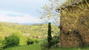 A stone building with a sloped roof, surrounded by lush greenery and a hilly landscape. - Une Sorcière sur le toit - Gîte** en Aveyron: Countryside and absolute tranquillity! (Firmi)