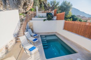 Una piscina con escalones de acceso, rodeada de paredes blancas y una cerca de madera.