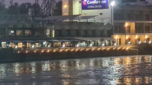 A Comfort Inn hotel with a signboard, waterfront view, and a reflection on the water. - Comfort Inn Coral River (Pathankot)