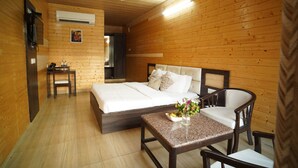 A wooden-paneled room with a bed, a table with a vase of flowers, and a chair. - Comfort Inn Coral River (Pathankot)