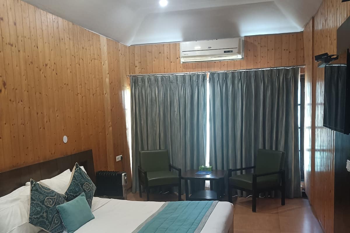 Una habitación de hotel con cama, dos sillas, una mesa, aire acondicionado y televisión.
