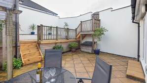 A patio with a table, chairs, and a bottle of wine. There is a wooden staircase and a railing. - Lavender - Two Bedroom Cottage, Sleeps 4 (Wadebridge)