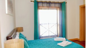 Une chambre d’hôtel avec un lit, une lampe, une fenêtre avec des rideaux et une porte.