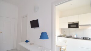 Une cuisine moderne avec des meubles blancs, un four à micro-ondes et un évier. On y trouve une lampe bleue posée sur une table blanche et un téléviseur fixé au mur.