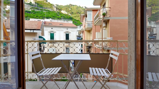 Un balcon avec une table et des chaises, donnant sur une colline parsemée de bâtiments.