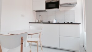 Une cuisine compacte avec des meubles blancs, un plan de travail noir, une hotte en acier inoxydable et un petit coin repas avec deux chaises.