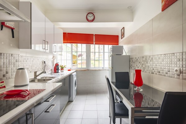 A modern kitchen with a sink, a washing machine, and a dining area with a red chair and table.