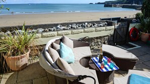 A patio with wicker furniture, a table with a checkered tablecloth, and a view of the beach and sea.